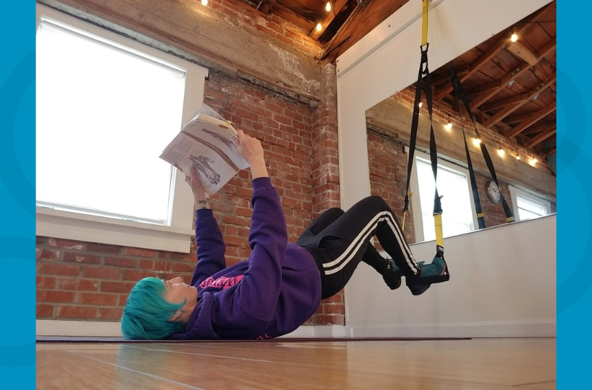 Mona is doing a TRX hip thrust while reading a heavy textbook